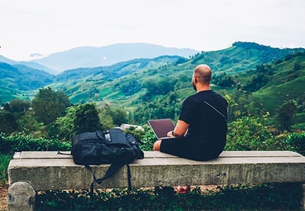 Man Editing a website on a bench overlooking mountains